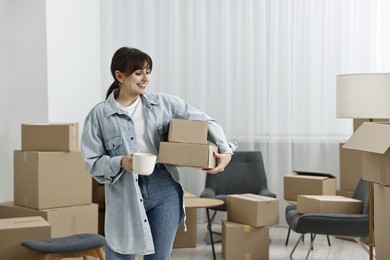 Photo of Moving day. Happy woman with cup of drink and cardboard boxes in her new home, space for text