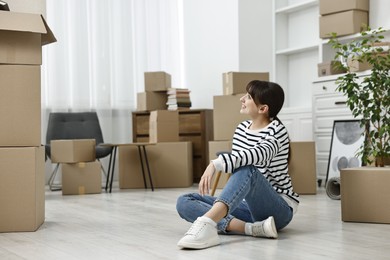 Photo of Moving day. Happy woman resting on floor and cardboard boxes in her new home