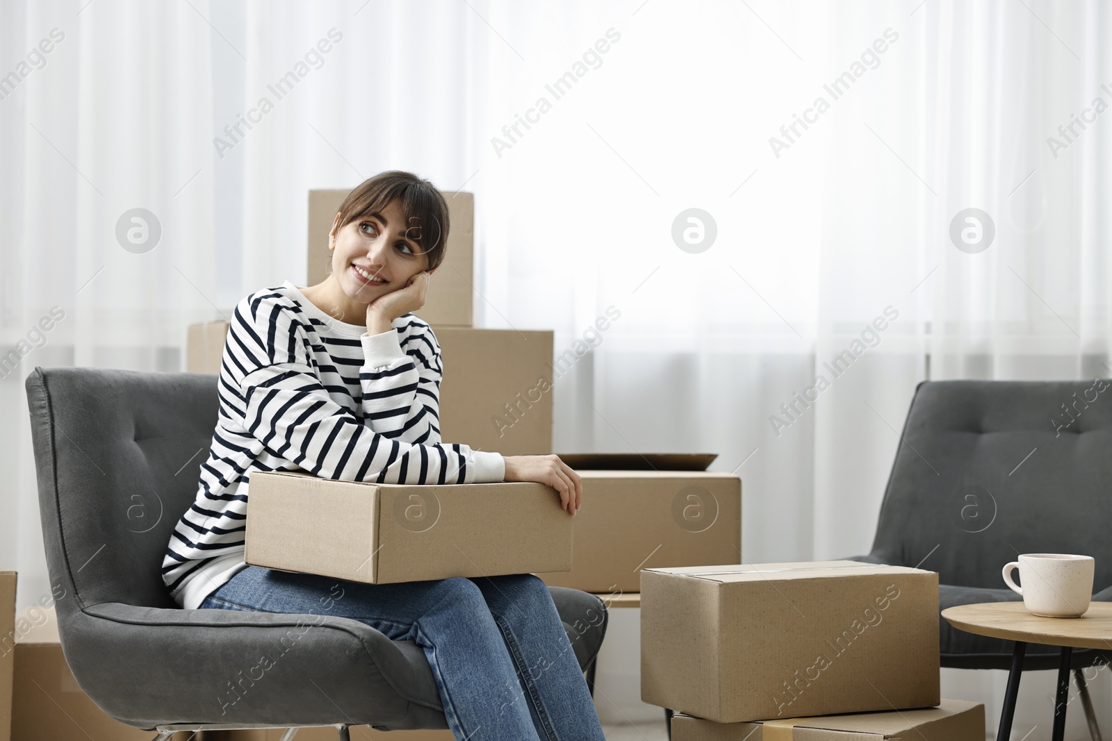 Photo of Moving day. Happy woman with cardboard box in her new home