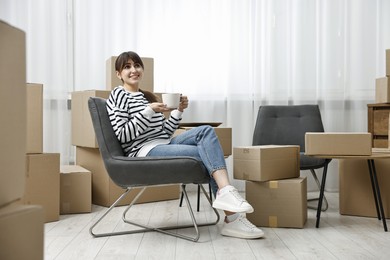 Moving day. Happy woman with cup of drink and cardboard boxes in new home