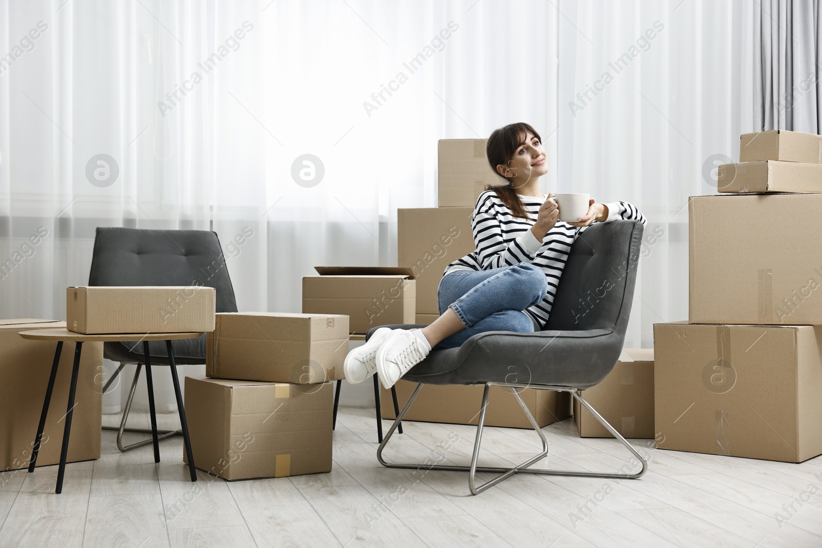 Photo of Moving day. Woman with cup of drink and cardboard boxes in new home