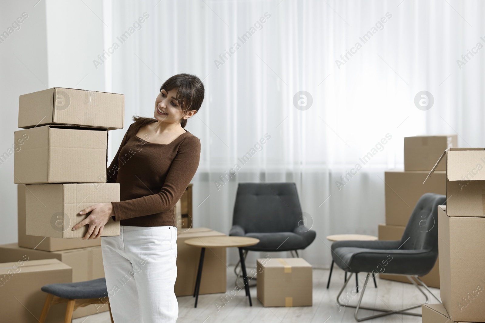 Photo of Moving day. Happy woman with cardboard boxes in her new home