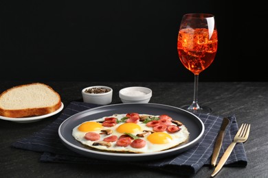 Photo of Tasty brunch. Delicious fried eggs with sausage and aperol cocktail served on black table