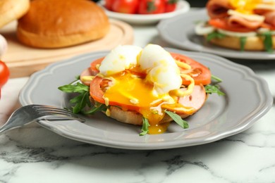 Photo of Tasty brunch. Poached egg, ham, tomato, arugula and bun on white marble table, closeup