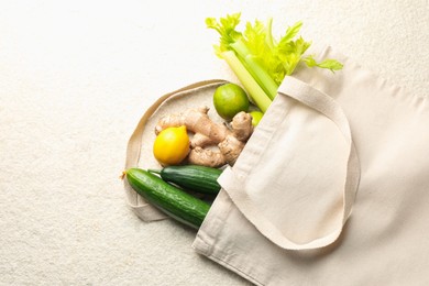 Photo of Eco bag with vegetables, fruits and ginger on white textured table, top view. Space for text