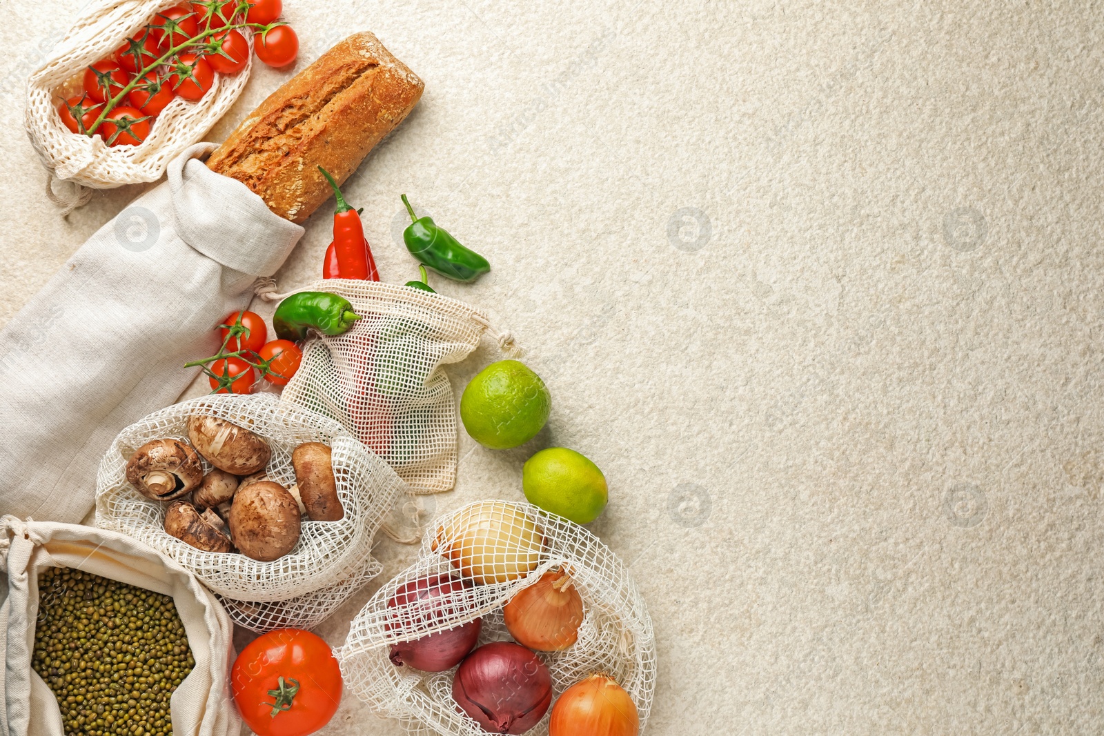 Photo of Eco bags with different food products on white textured table, flat lay. Space for text