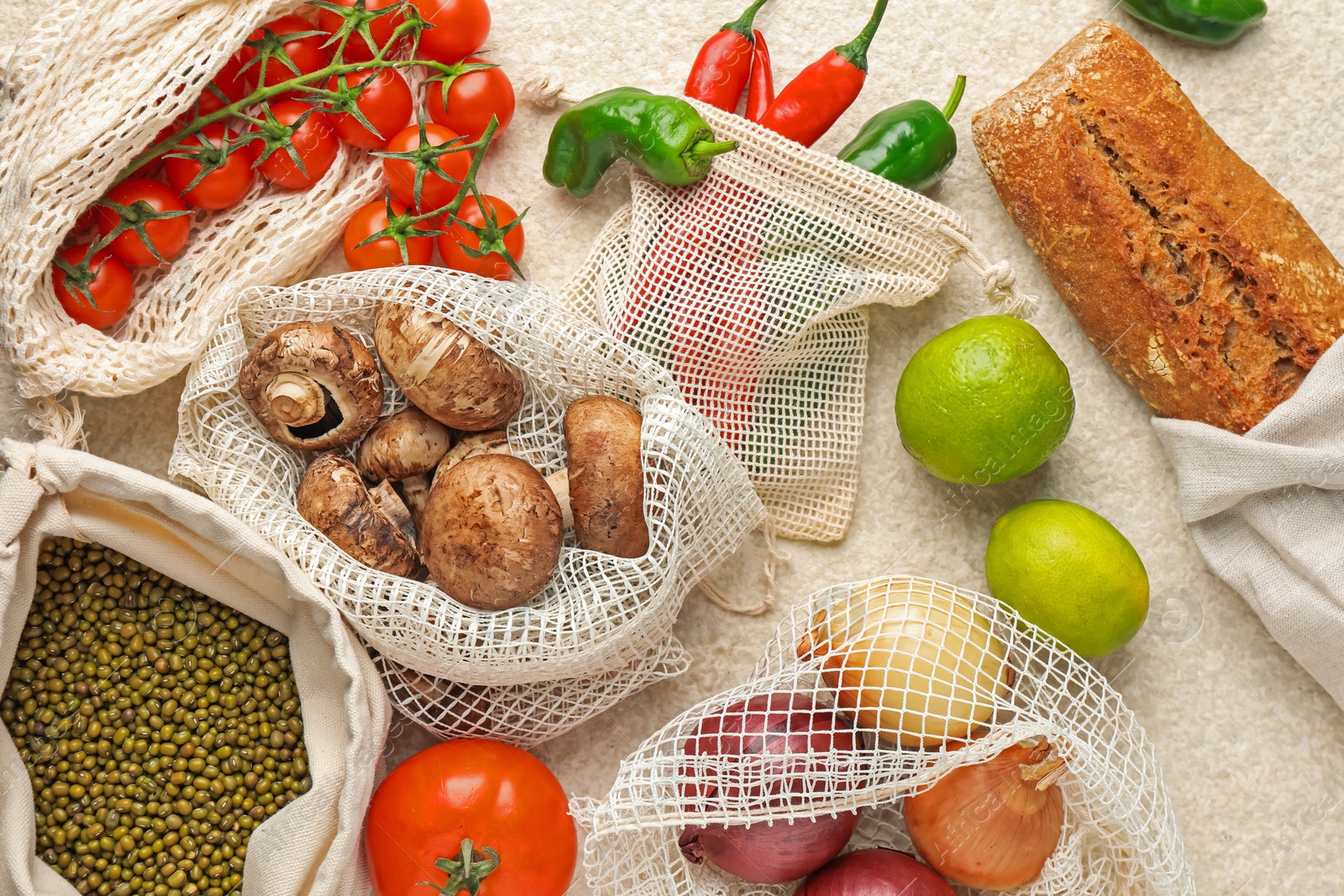 Photo of Eco bags with different food products on white textured table, flat lay