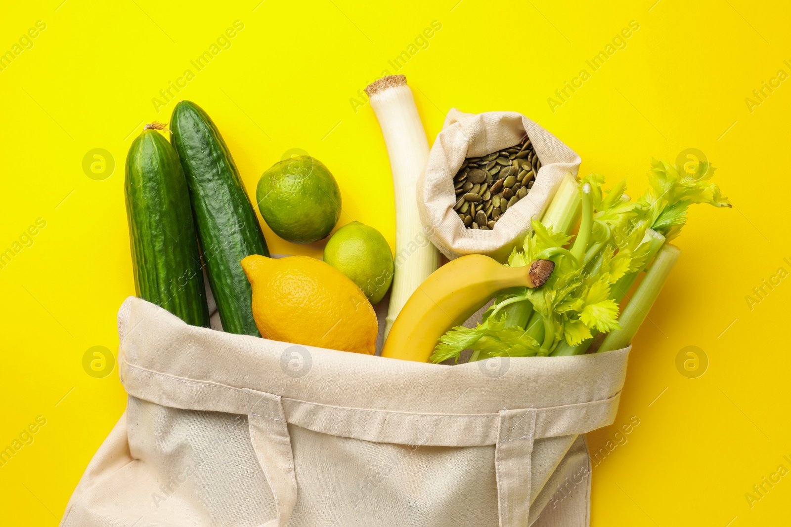 Eco bag with vegetables, fruits and pumpkin seeds on yellow background, top view Photo of Eco bag with vegetables, fruits and pumpkin seeds on yellow background, top view