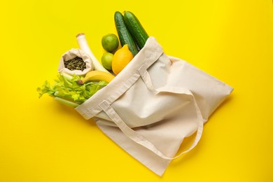 Photo of Eco bag with vegetables, fruits and pumpkin seeds on yellow background, top view