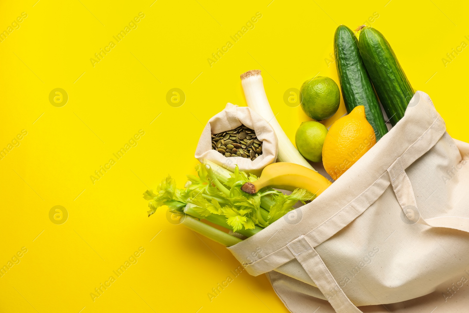 Photo of Eco bag with vegetables, fruits and pumpkin seeds on yellow background, top view. Space for text