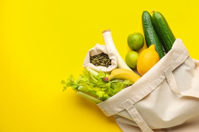 Photo of Eco bag with vegetables, fruits and pumpkin seeds on yellow background, top view. Space for text