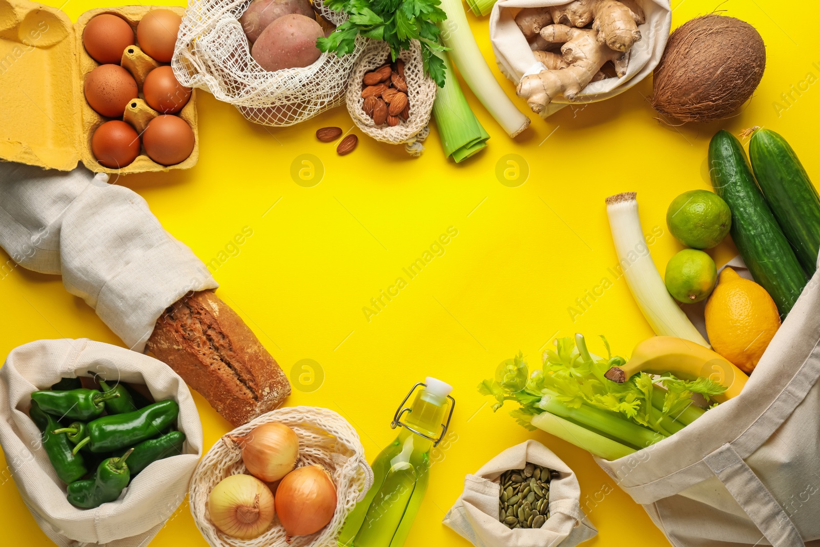 Photo of Frame of eco bags with different food products on yellow background, flat lay. Space for text