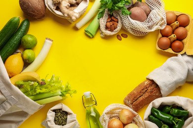 Photo of Frame of eco bags with different food products on yellow background, flat lay. Space for text