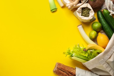 Photo of Eco bags with different food products on yellow background, flat lay. Space for text