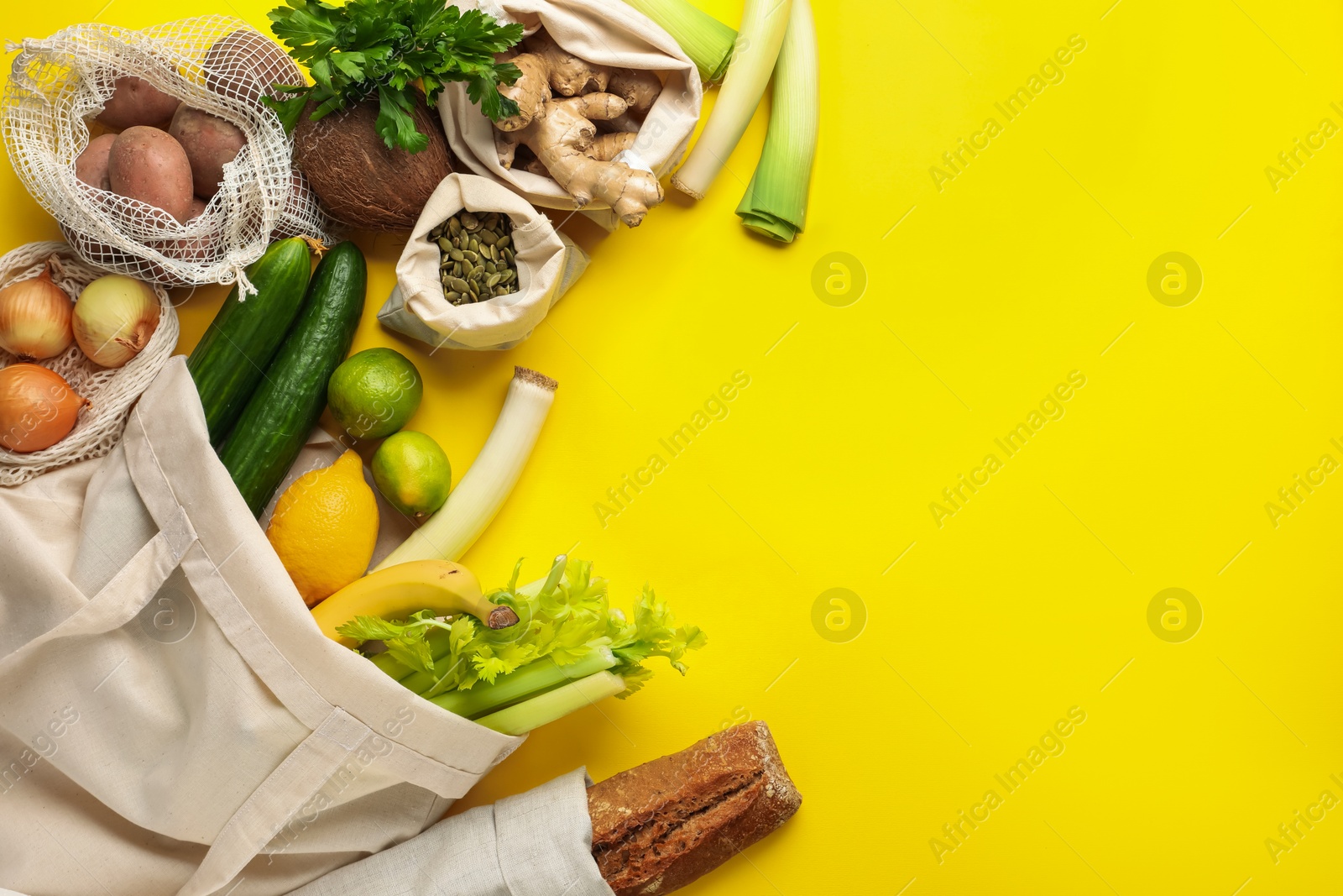 Photo of Eco bags with different food products on yellow background, flat lay. Space for text