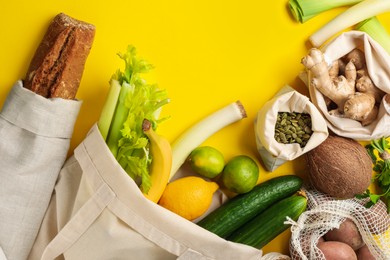 Photo of Eco bags with different food products on yellow background, flat lay