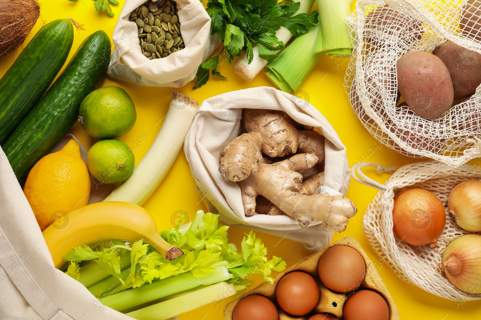 Photo of Eco bags with different food products on yellow background, flat lay