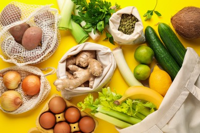 Photo of Eco bags with different food products on yellow background, flat lay