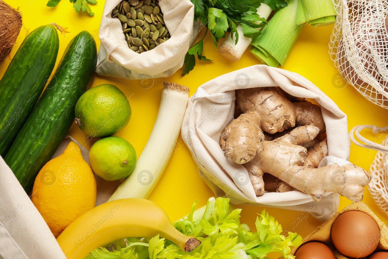 Photo of Eco bags with different food products on yellow background, flat lay