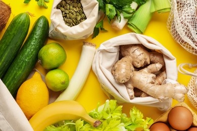 Photo of Eco bags with different food products on yellow background, flat lay