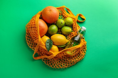 Photo of Eco bag with fruits and bottle of drink on green background, top view