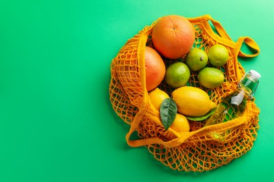 Photo of Eco bag with fruits and bottle of drink on green background, top view. Space for text