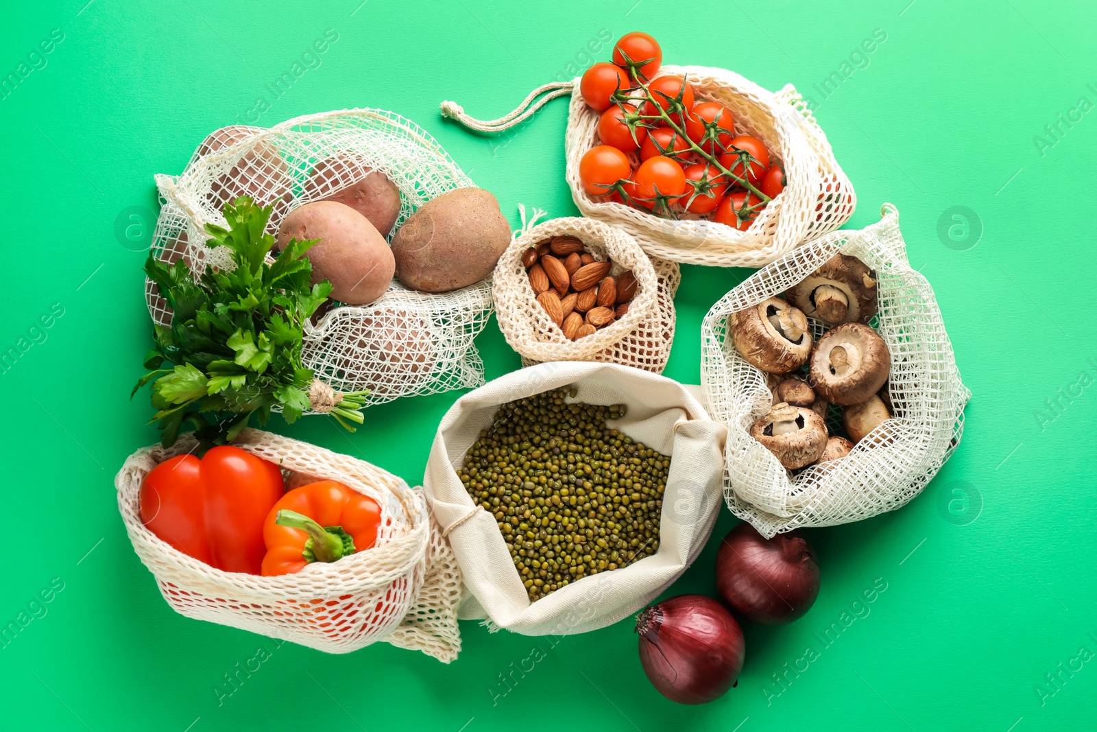 Photo of Eco bags with different food products on green background, flat lay