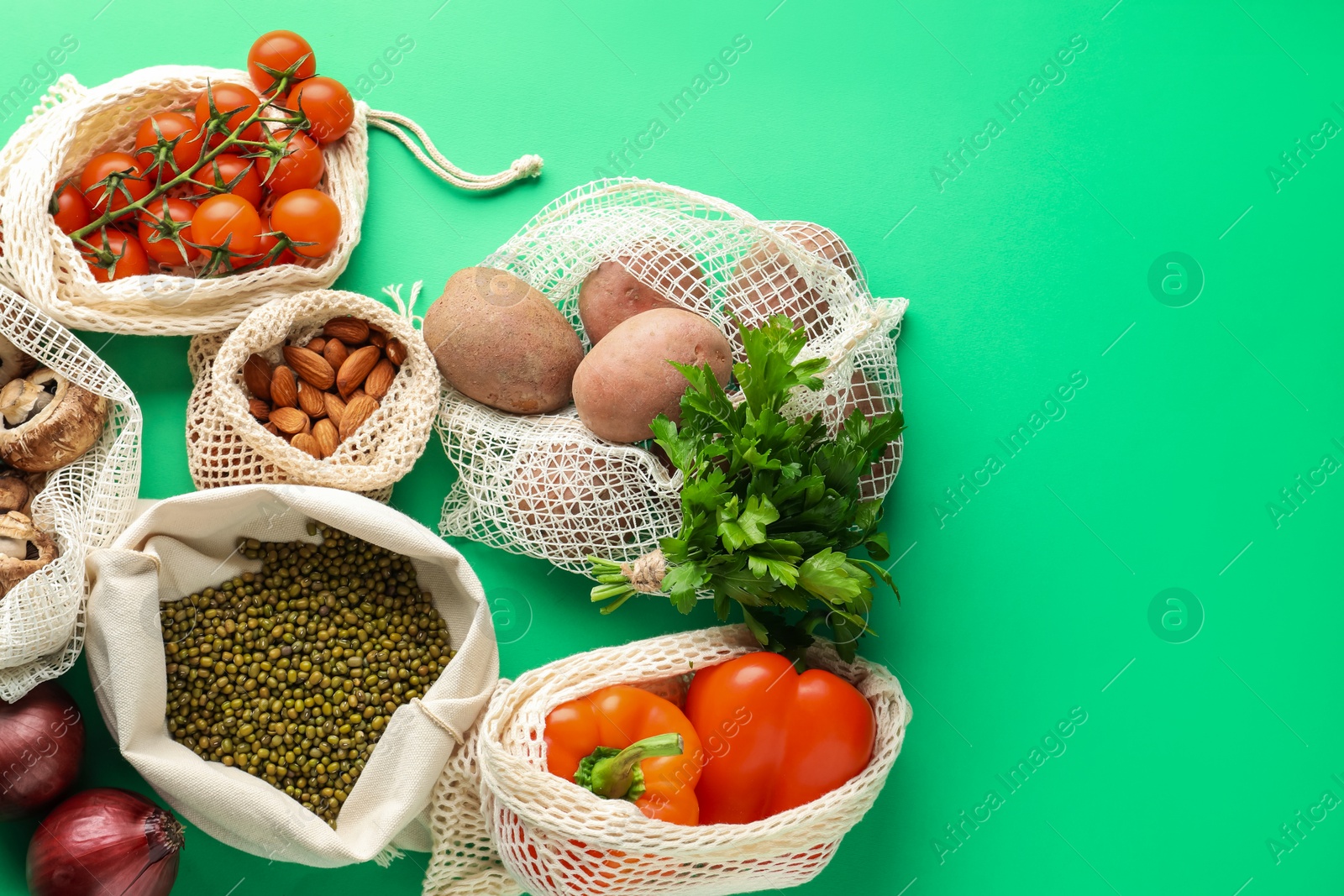 Photo of Eco bags with different food products on green background, flat lay. Space for text