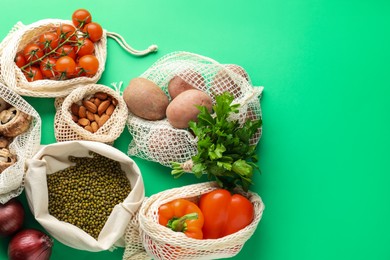 Photo of Eco bags with different food products on green background, flat lay. Space for text