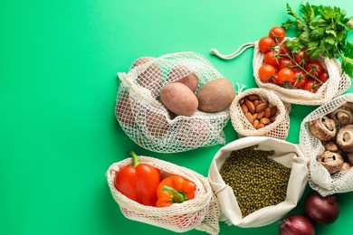 Photo of Eco bags with different food products on green background, flat lay. Space for text