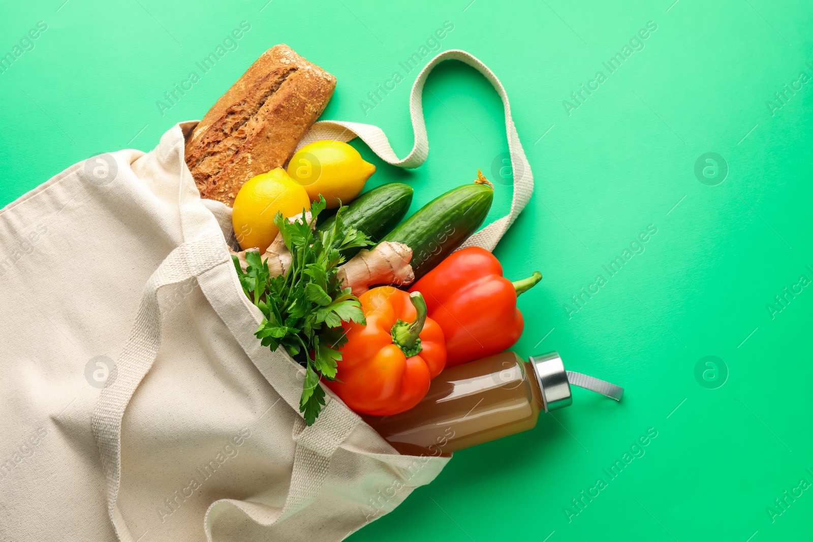 Photo of Eco bag with different food products and juice on green background, top view. Space for text