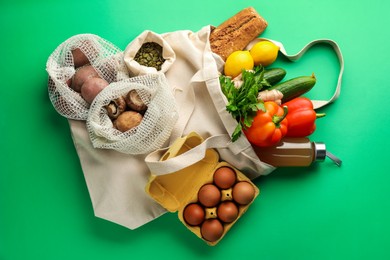 Photo of Eco bags with different food products on green background, flat lay