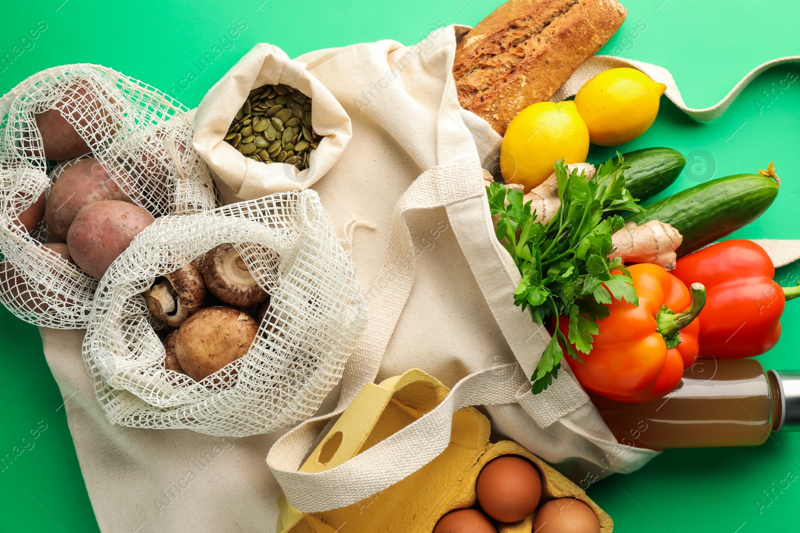 Photo of Eco bags with different food products on green background, flat lay