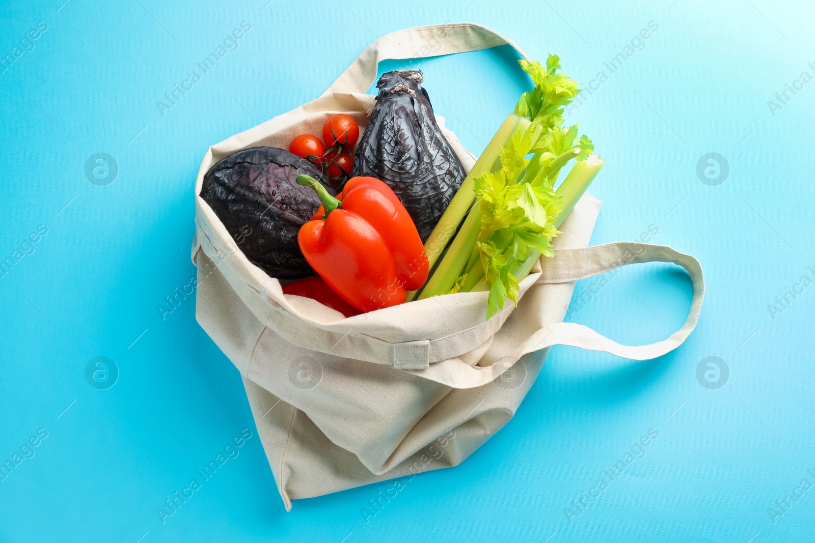 Photo of Eco bag with different vegetables on light blue background, top view