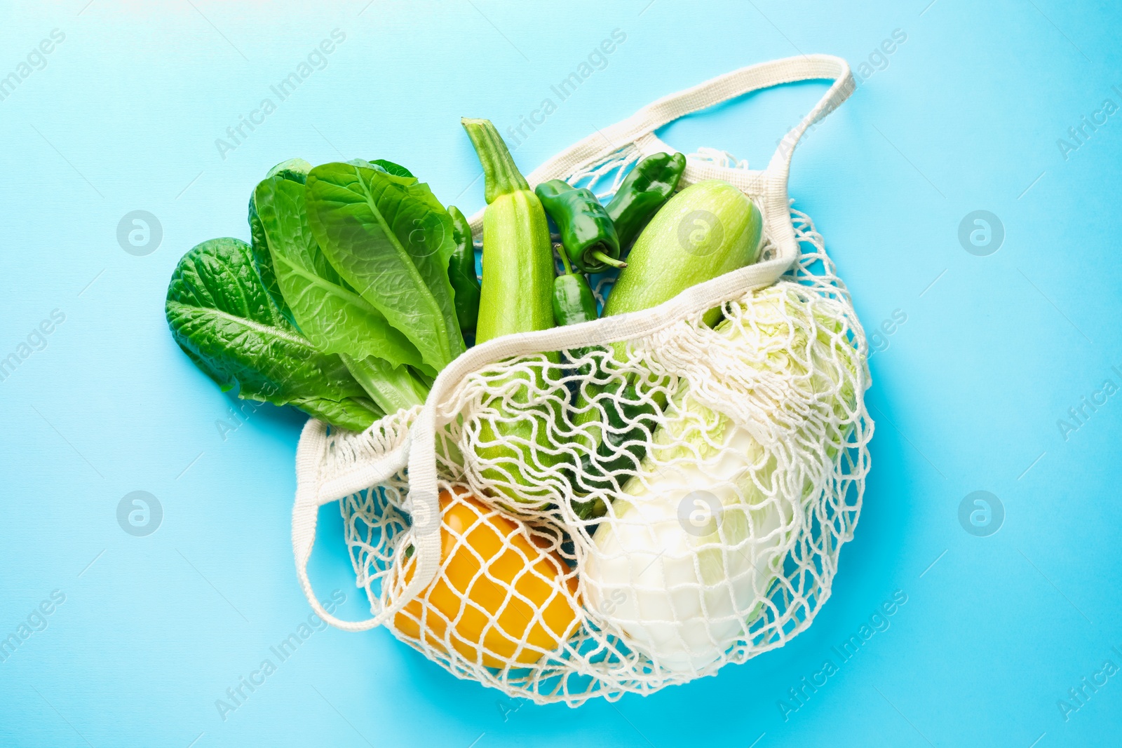 Photo of Net bag with products on light blue background, top view. Eco friendly lifestyle