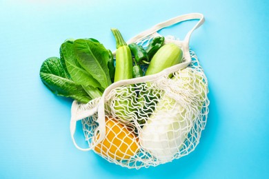 Photo of Net bag with products on light blue background, top view. Eco friendly lifestyle