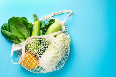 Photo of Net bag with products on light blue background, top view and space for text. Eco friendly lifestyle