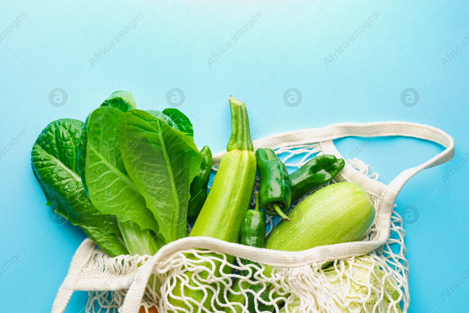 Photo of Net bag with products on light blue background, top view and space for text. Eco friendly lifestyle