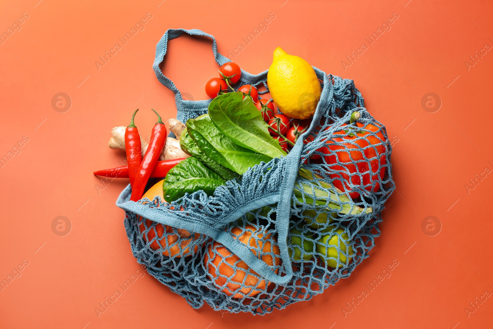 Photo of Net bag with products on orange background, top view. Eco friendly lifestyle