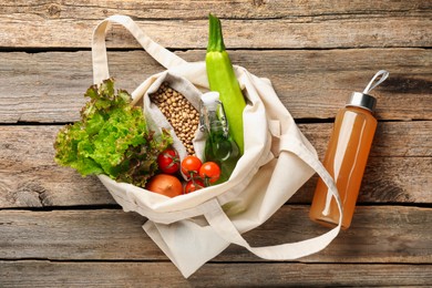 Photo of Shopper bag with products on wooden background, top view. Eco friendly lifestyle