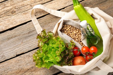 Photo of Shopper bag with products on wooden background, closeup. Eco friendly lifestyle