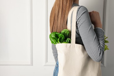 Photo of Woman holding shopper bag with groceries near white wall, closeup and space for text. Eco friendly lifestyle