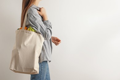 Photo of Woman holding shopper bag with groceries on white background, closeup and space for text. Eco friendly lifestyle