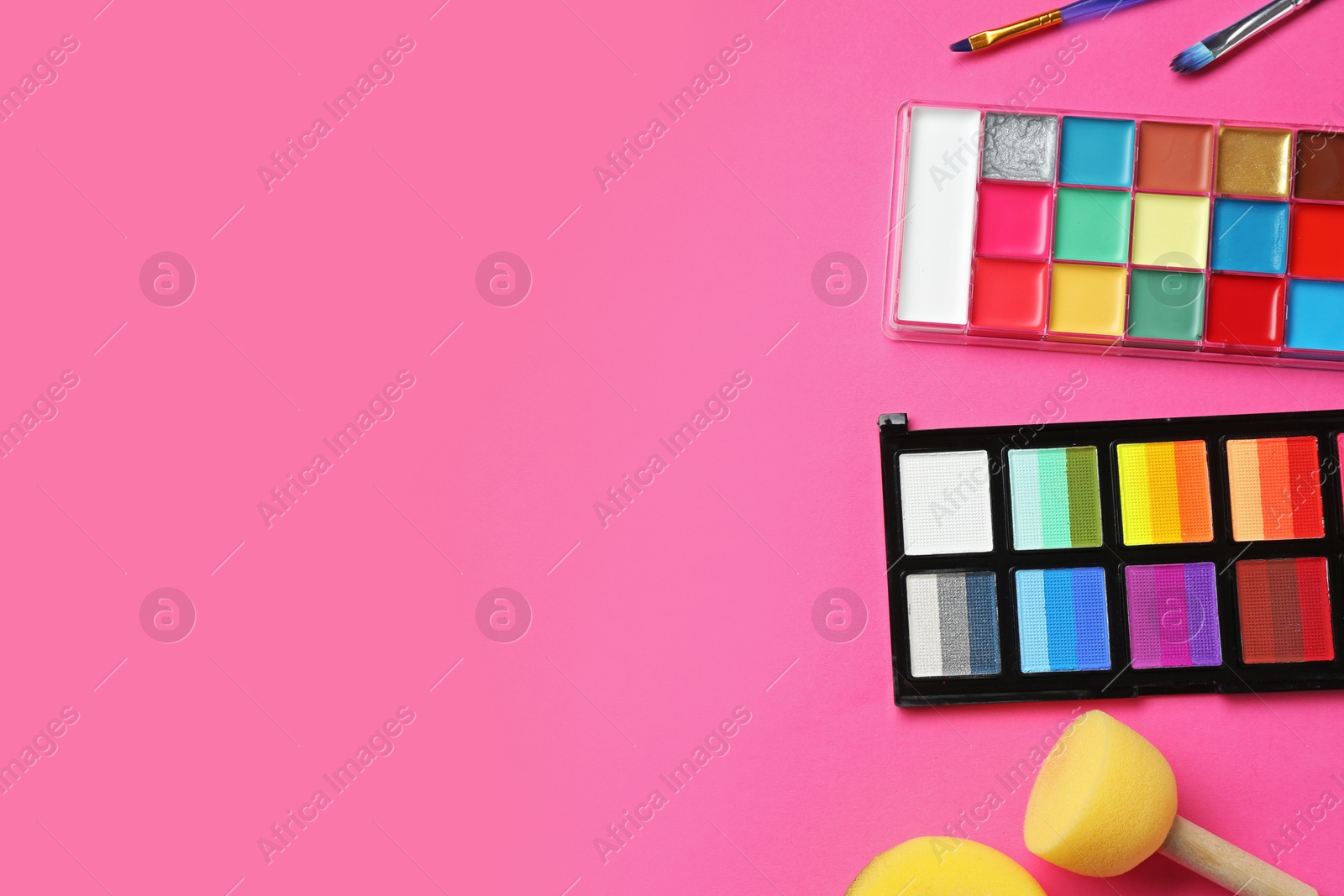 Bright face paints, brushes and sponges on pink background, flat lay. Space for text Photo of Bright face paints, brushes and sponges on pink background, flat lay. Space for text