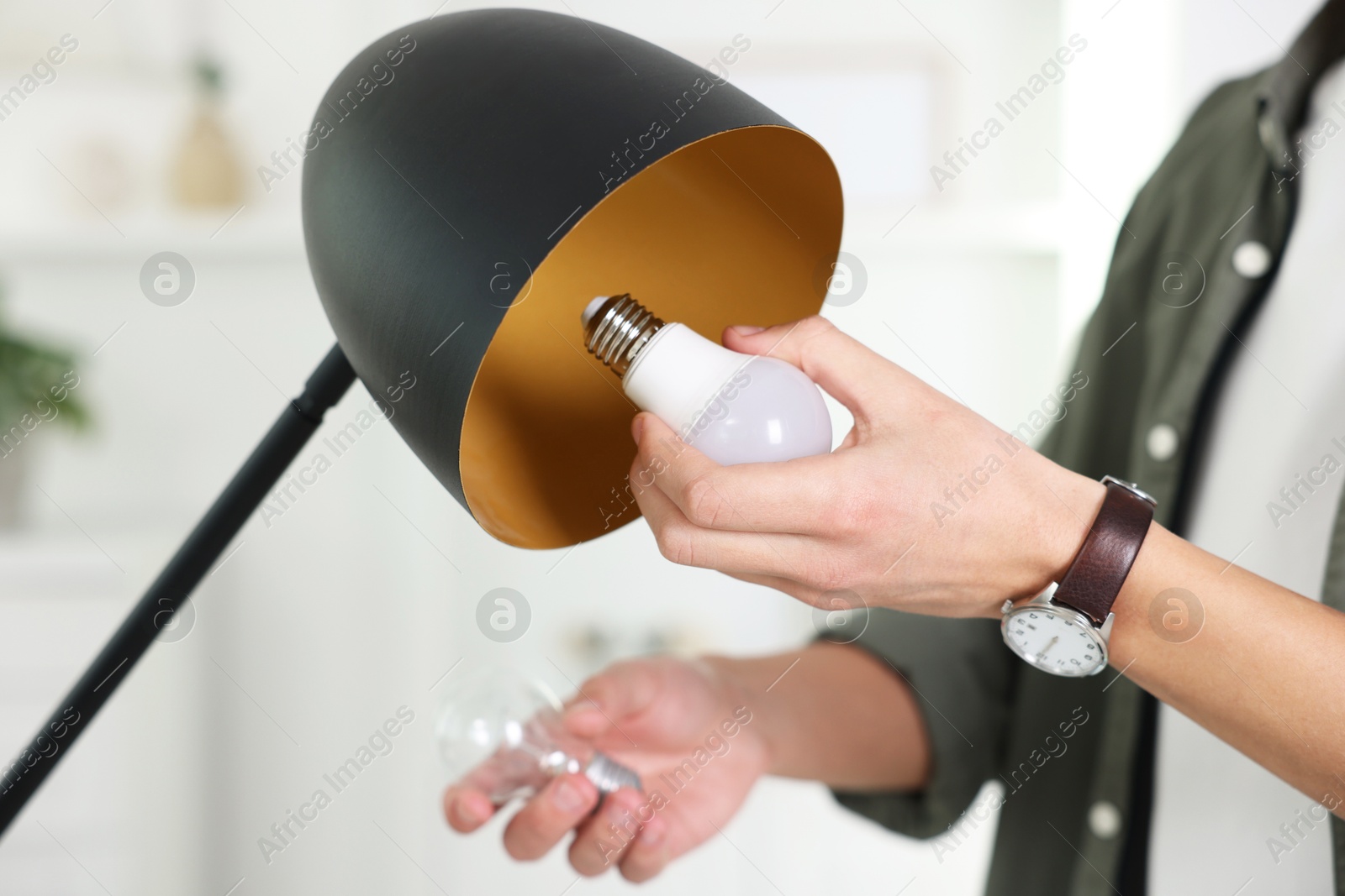 Photo of Man changing incandescent light bulb for fluorescent one in lamp at home, closeup