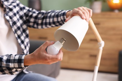 Photo of Man changing light bulb in lamp at home, closeup