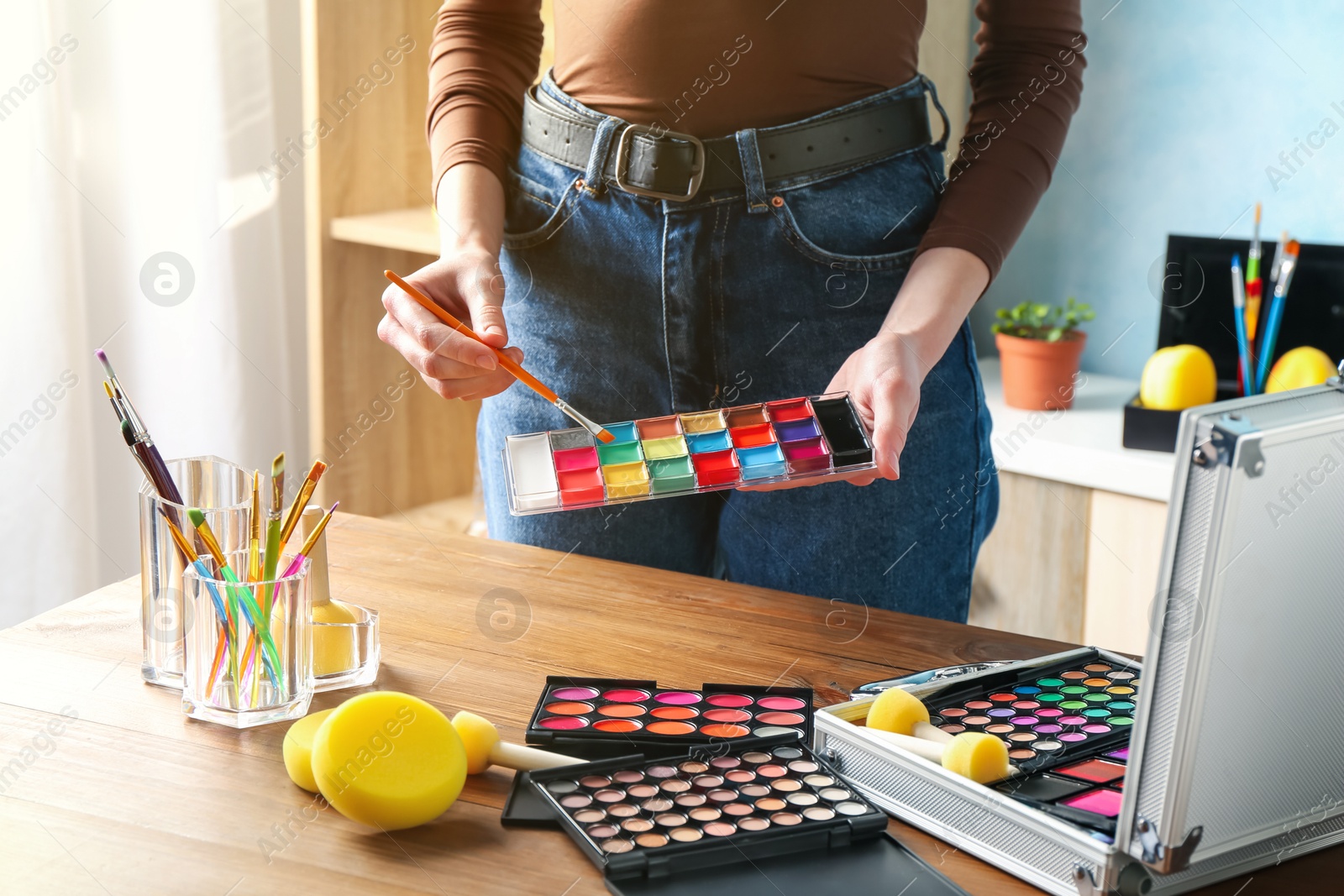 Professional artist with face painting products and tools at wooden table, closeup Photo of Professional artist with face painting products and tools at wooden table, closeup