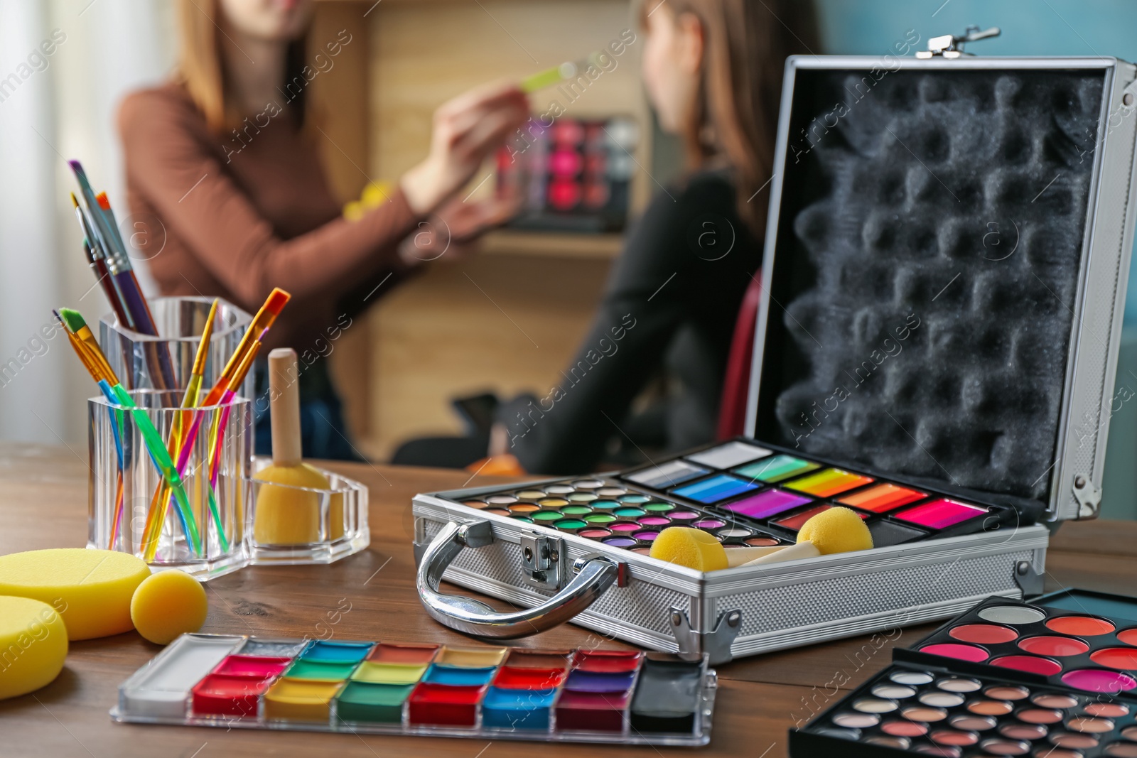 Photo of Face paints on wooden table and artist working with client indoors, selective focus