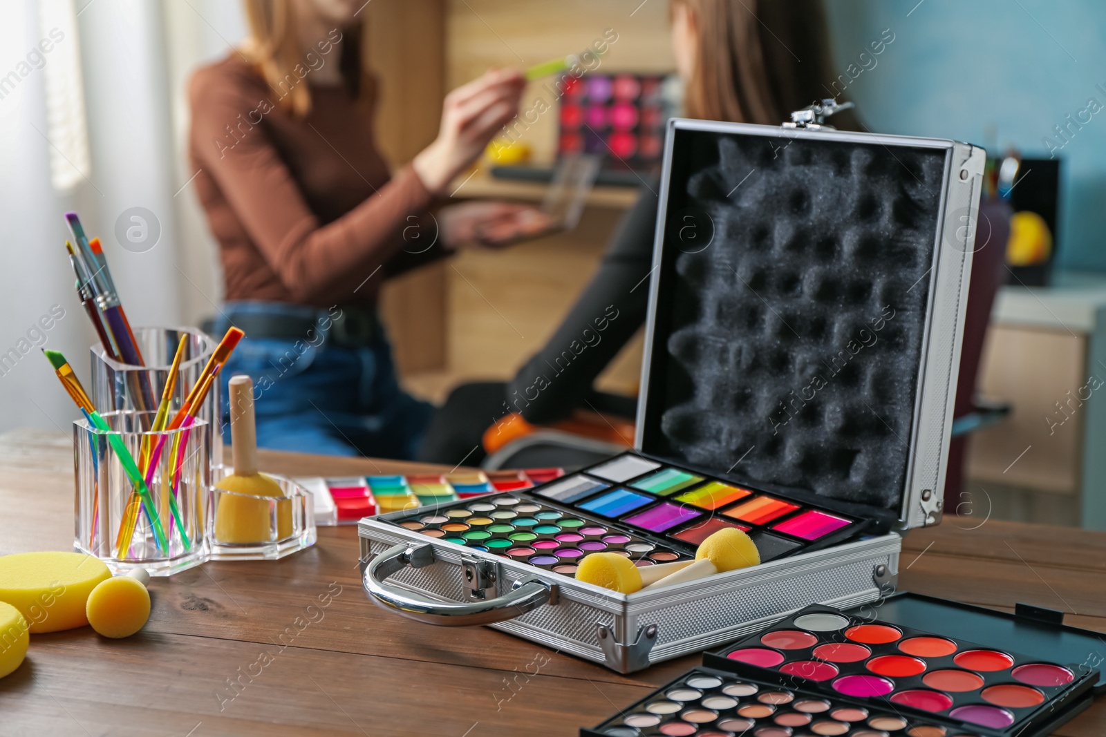 Face paints on wooden table and artist working with client indoors, selective focus Photo of Face paints on wooden table and artist working with client indoors, selective focus