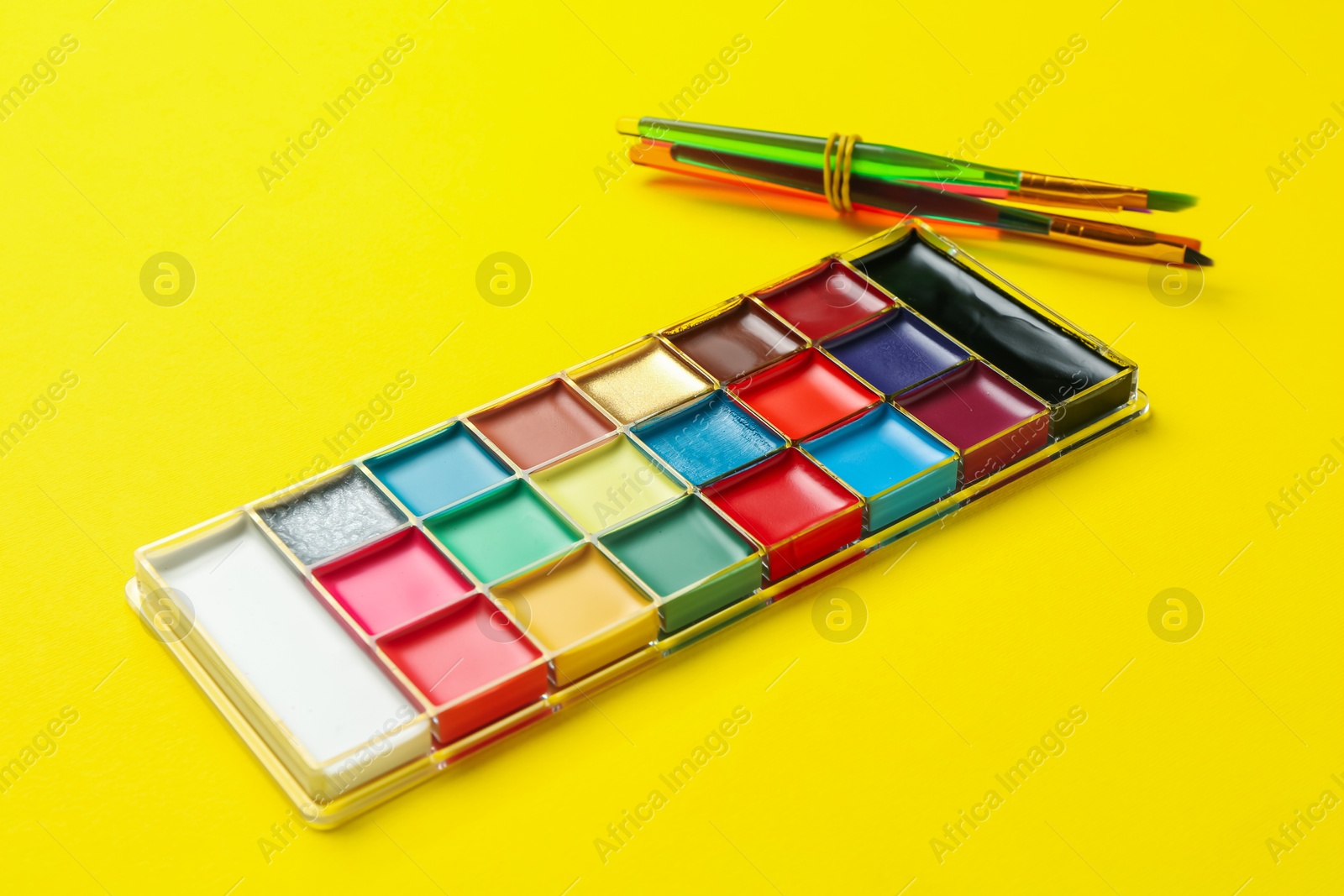 Face paint palette and brushes on yellow background, closeup Photo of Face paint palette and brushes on yellow background, closeup